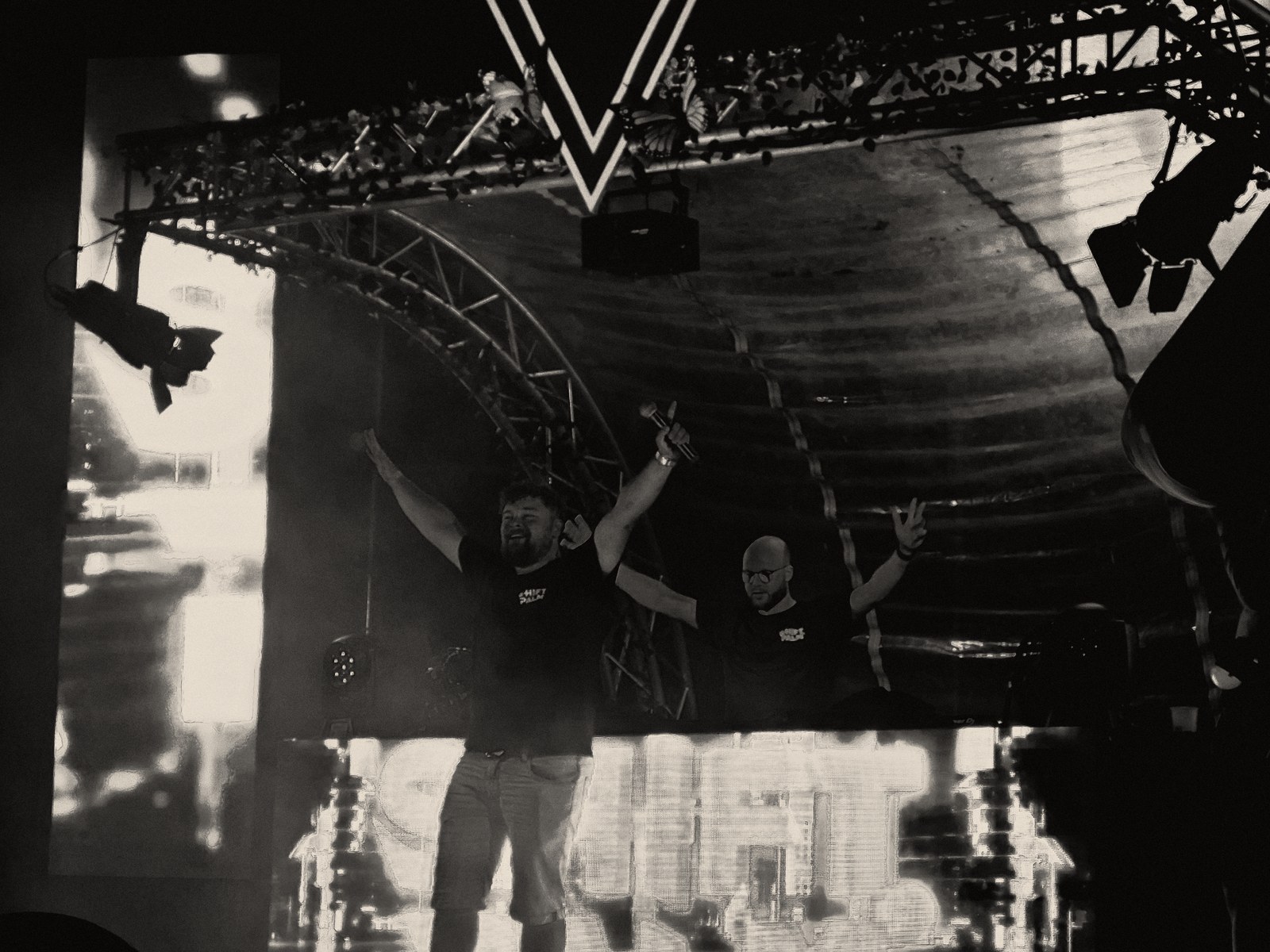Shift & Palm performing live on stage, both with arms raised in front of the crowd